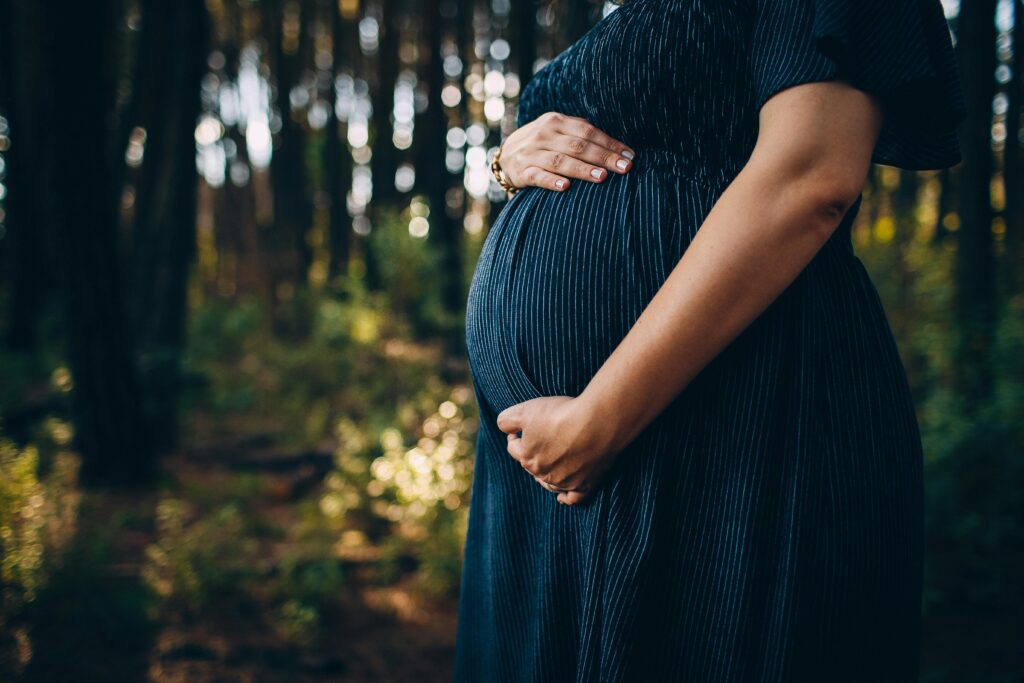 A peaceful moment of a pregnant woman embracing nature in a sunlit forest.
